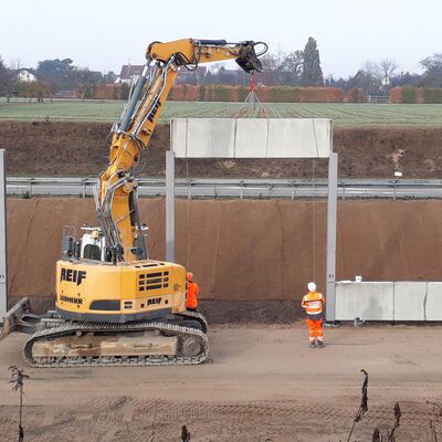 Bagger setzt Schallschutzwand in Fassung ein.