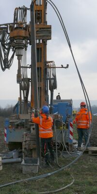 Ein Bohrbagger wird von zwei Arbeiter:innen gesteuert.