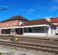 Ein Bahnhof mit Bahnhofsgebäude und Bushaltestelle an der Seite.