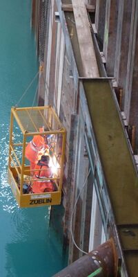 Zwei Arbeiter:innen schweißen an einem Becken voller Wasser.
