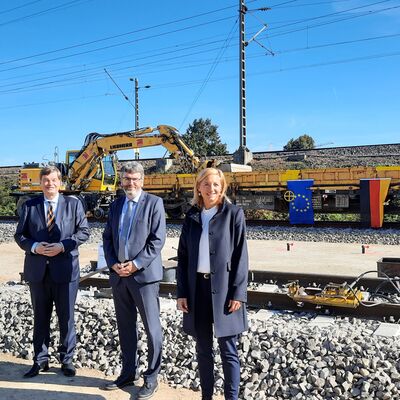 Vier Menschen, im Hintergrund ein Güterwagen mit den Flaggen der EU, Deutschlands und der Schweiz.