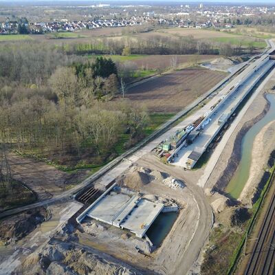 Ein Graben zwischen einer Baustelle und Bahngleisen.