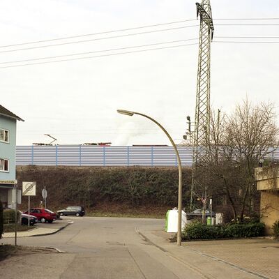 Ein Güterzug fährt hinter einer Schallschutzwand an Häusern vorbei.