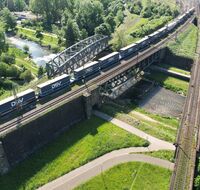 Eine Eisenbahnbrücke über einen Fluss. Eine Eisenbahn fährt gerade drüber.