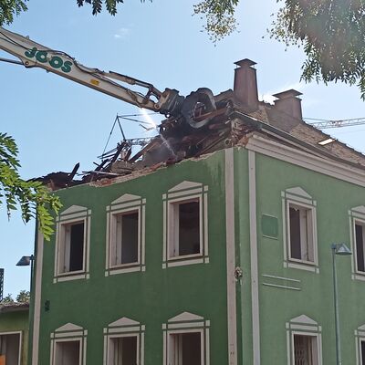 Ein grünes Gebäude, dessen Dach durch einen Bagger abgerissen wird.
