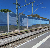 Ein Bahnsteig mit Gleisen und einer hohen Lärmschutzwand, die mit einem blauen und schwarzen Bergmotiv bemalt ist.