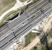 Luftaufnahme einer viergleisigen Bahnstrecke mit einem Tierdurchlass unter den Gleisen, umgeben von Grünflächen.