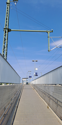 Eine gepflasterte Rampe mit Geländern führt zum Bahnsteig.