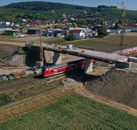 Ein roter Zug fährt unter eine Straßenüberführung durch.