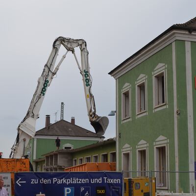 Ein grünes Bahnhofsgebäude und links daneben steht ein Bagger.