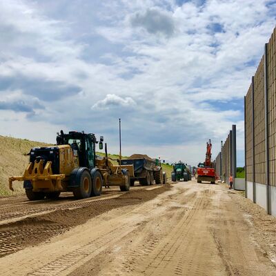 Baustellenfahrzeuge stehen entlang einer Schallschutzwand.