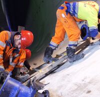 Zwei Arbeiter:innen verbinden große blaue Rohre im Tunnel.