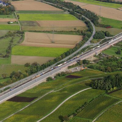 Eine zweispurige Autobahn und zwei Gleise führen durch eine Feldlandschaft.