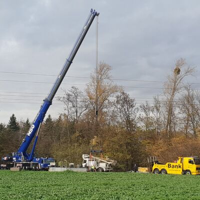 Ein großer Kran hebt ein Baustellenfahrzeug neben einem Feld an.