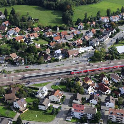Ein roter Zug fährt in einen Bahnhof mitten in einem Dorf ein.