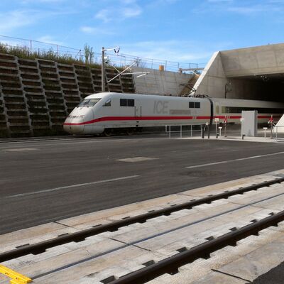 Ein weißer Zug fährt aus einem Tunnelportal des Katzenbergtunnels raus.