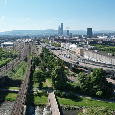 Im Vordergrund eine Eisenbahnbrücke, im Hitergrund eine Stadt
