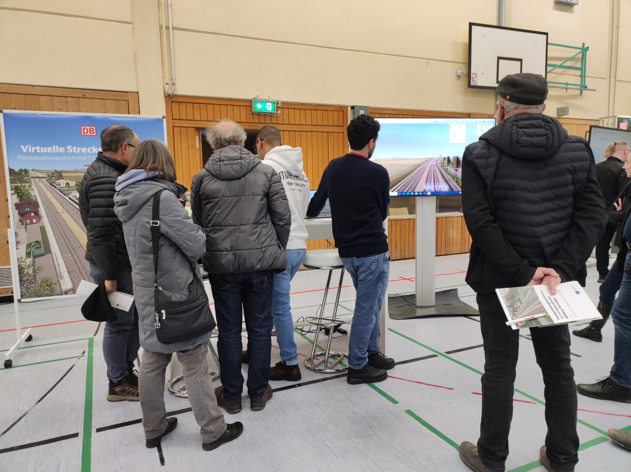 Menschen stehen vor Monitor, auf dem ein Streckenverlauf animiert ist.