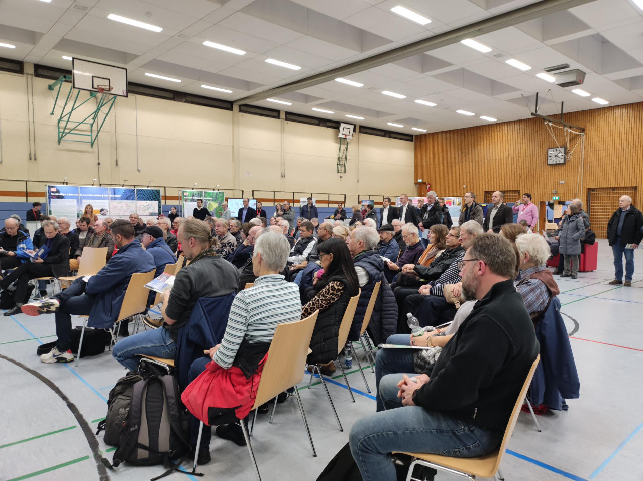 Menschen sitzen in einer Turnhalle auf Stühlen