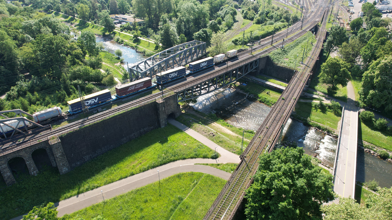 Zwei Brücken, die über einen Fluss führen. Auf der einen fährt ein Güterzug.