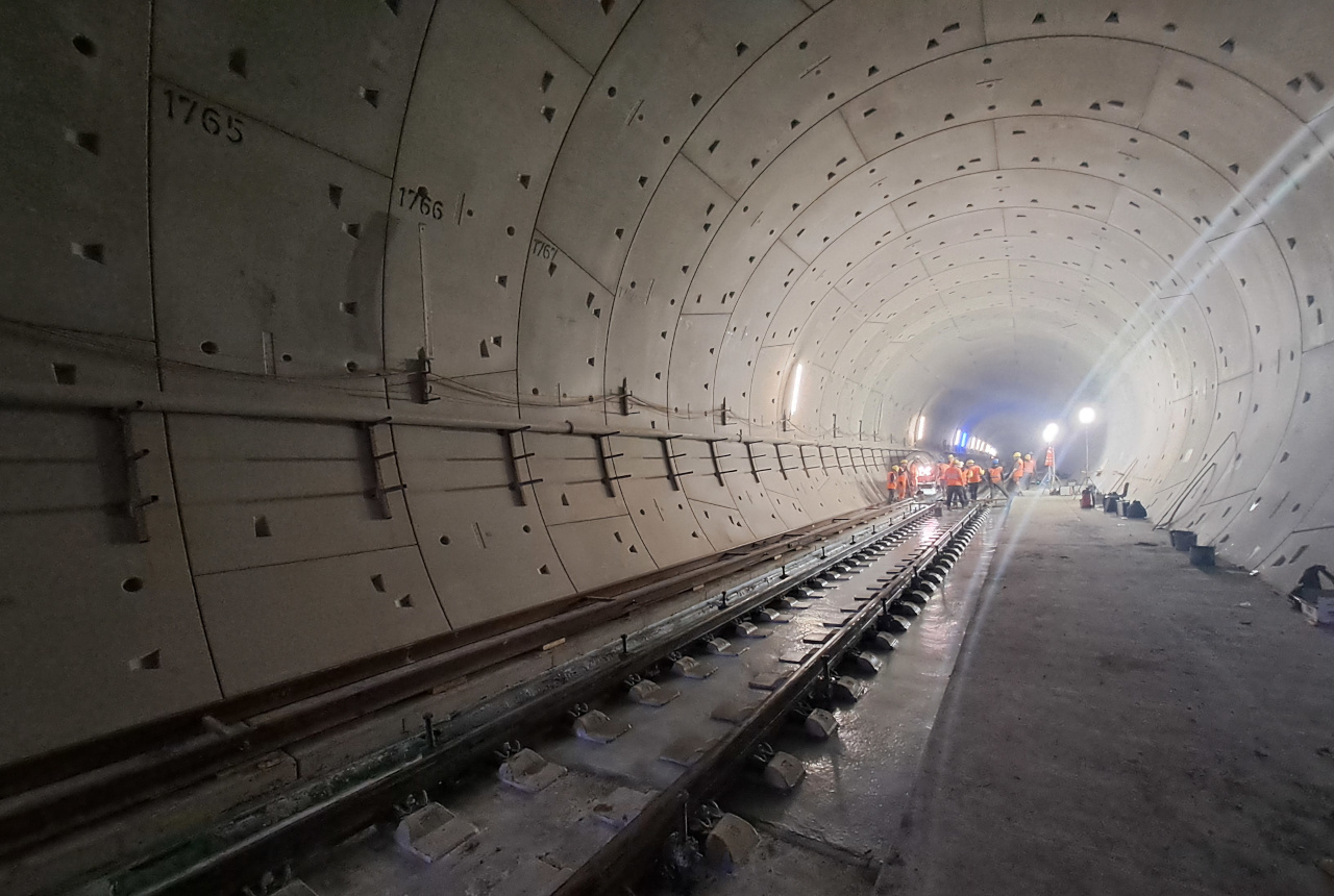 Innenansicht eines Tunnels. Personen tragen Warnwesten und Helme und befinden sich im Tunnel.